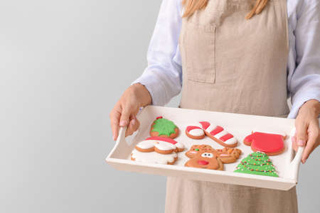 Woman with tasty Christmas cookies on tray against gray background, closeup