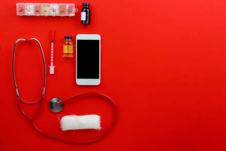 Modern mobile phone with doctor's supplies on color background