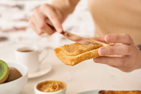 Woman spreading tasty peanut butter onto toasted bread, closeup