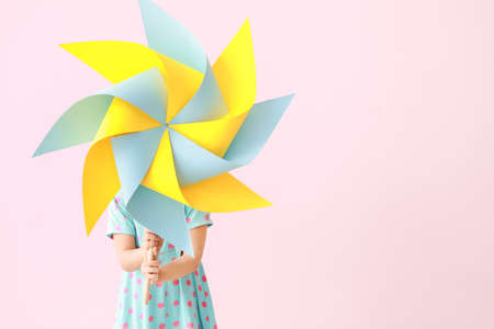 Cute little girl with paper windmill on color background