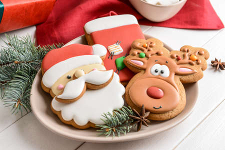 Plate with tasty Christmas cookies on white wooden table