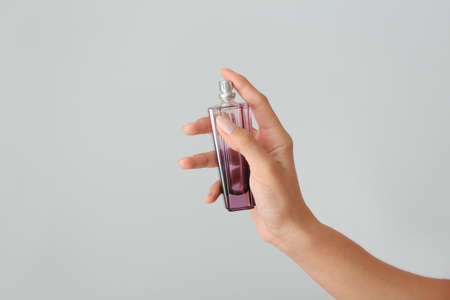 Female hand with bottle of perfume on light background