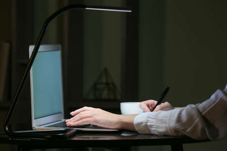 Woman working on laptop at table in eveningの写真素材