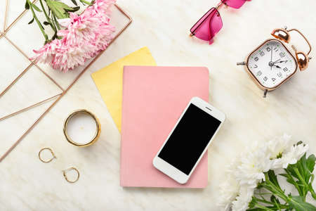 Modern mobile phone with notebook and female accessories on light background
