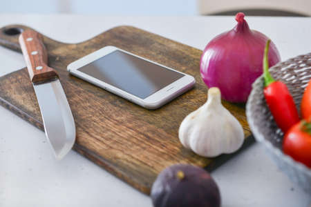 Modern mobile phone with knife, cutting board and fresh products on tableの写真素材