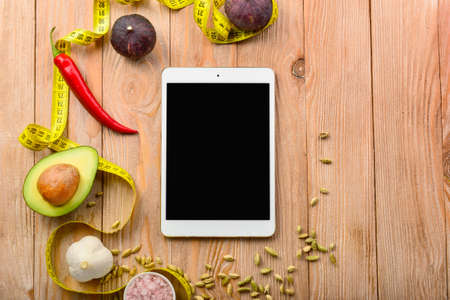 Modern tablet computer with fresh products and measuring tape on wooden background