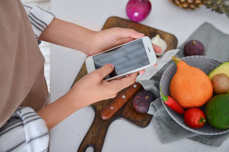 Woman using mobile phone while cooking on kitchen