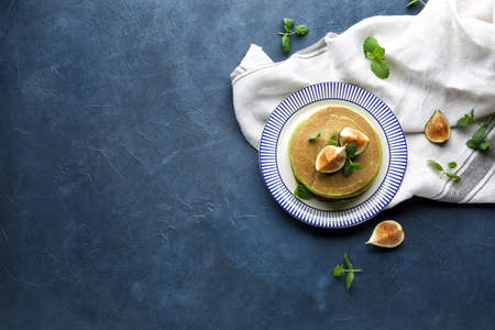 Plate with green pancakes and fig fruit on color background
