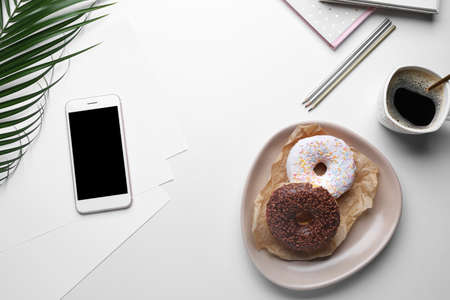 Tasty donuts with mobile phone, cup of coffee and stationery on white backgroundの写真素材