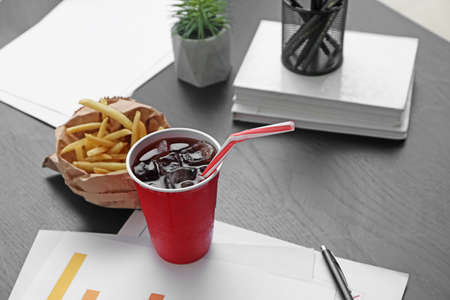 Cup of cold cola with french fries on table in office