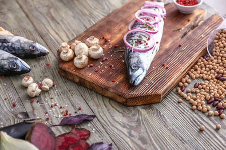 Raw mackerel fish with spices, beans and mushrooms on wooden table