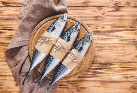 Board with raw mackerel fish on wooden background
