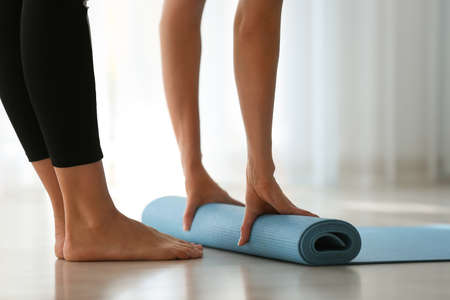 Young woman rolling yoga mat at homeの写真素材