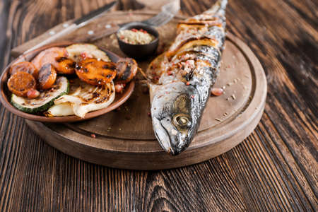 Board with prepared mackerel fish and vegetables on wooden background