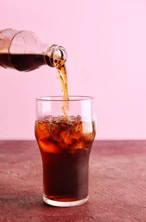 Pouring of cola from bottle into glass with ice on tableの写真素材