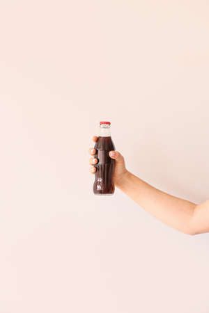 Female hand with bottle of cola on light backgroundの写真素材