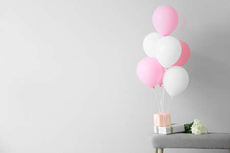 Air balloons with gift boxes and flowers on bench against light backgroundの写真素材