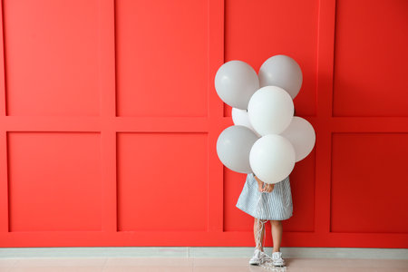 Little girl with balloons near color wallの写真素材