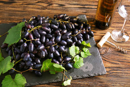 Slate plate with sweet grapes and bottle of wine on wooden table
