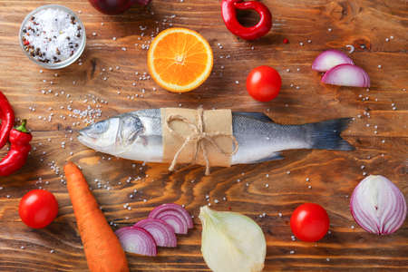 Fresh seabass fish, vegetables and spices on wooden background