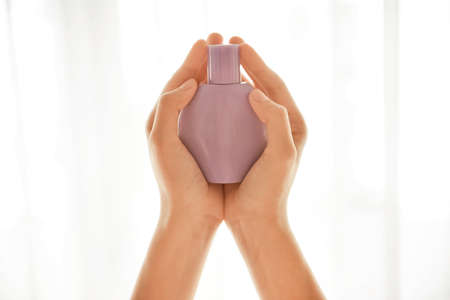 Female hands with bottle of perfume on light background