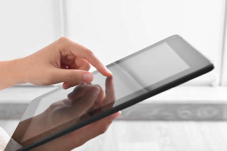 Young woman using modern tablet computer at home, closeup