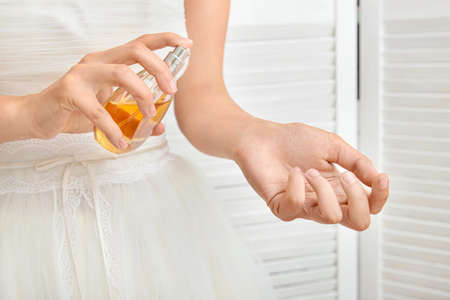 Beautiful young bride with bottle of perfume at home, closeup