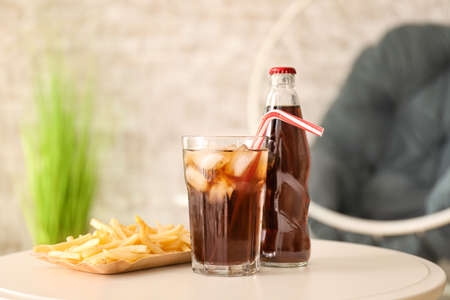 Glass, bottle of cold cola and french fries on table