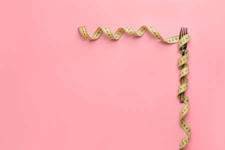 Fork with measuring tape on color background. Concept of dietの写真素材
