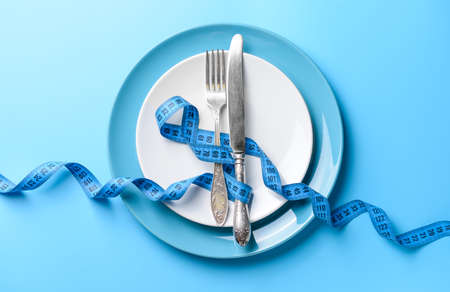 Cutlery with plates and measuring tape on color background. Concept of dietの写真素材