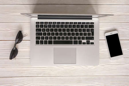 Modern laptop with mobile phone and sunglasses on wooden background