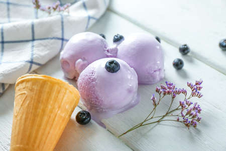Wafer cone with tasty blueberry ice cream on white table