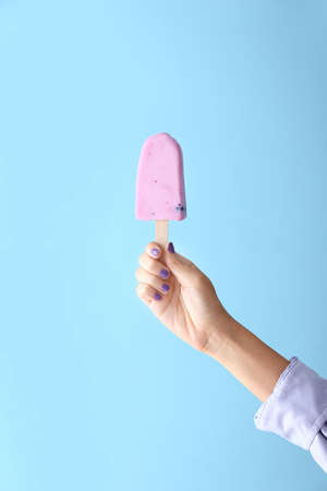 Female hand with tasty blueberry ice cream on color backgroundの写真素材