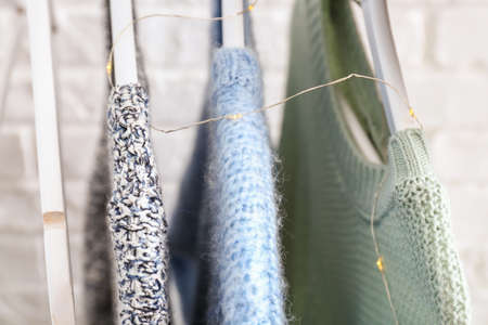 Hangers with winter clothes near white brick wall, closeup