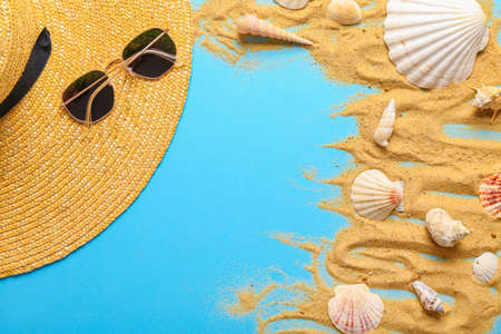 Summer composition with beach hat, sunglasses, sand and seashells on color backgroundの写真素材
