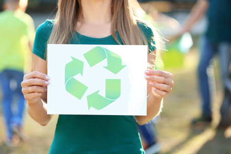 Woman holding paper sheet with symbol of recycling outdoorsの写真素材