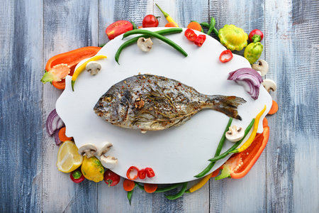 Board with prepared dorado fish and fresh vegetables on wooden tableの写真素材