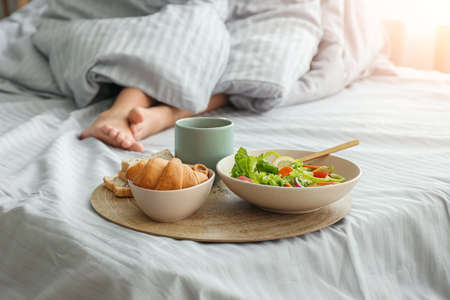 Woman with tasty breakfast lying in bed