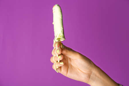 Female hand with tasty pistachio ice cream on color backgroundの写真素材