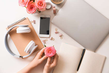 Female hands with beautiful rose flowers, laptop, mobile phone and headphones on white background