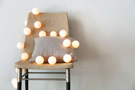 Chair with glowing garland and pillow on gray background