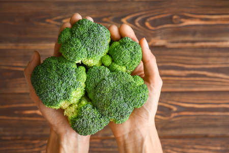 Female hands with fresh broccoli cabbage on wooden background, top view
