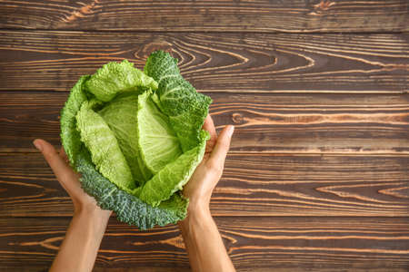 Female hands with fresh savoy cabbage on wooden background, top view