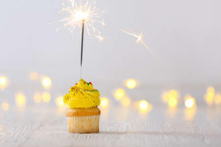 Tasty cupcake with sparkler on white table with blurred lightsの写真素材