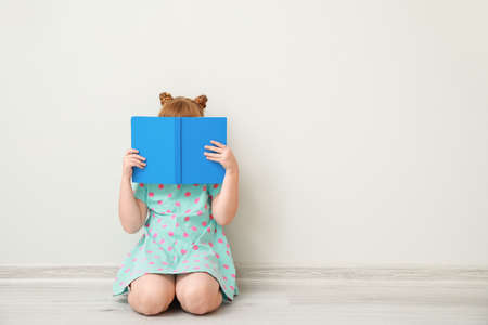 Cute little girl with book sitting near white wallの写真素材