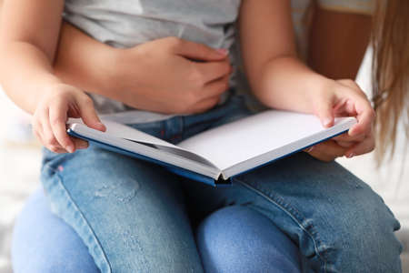 Beautiful young woman and her little daughter reading book at home, closeupの写真素材
