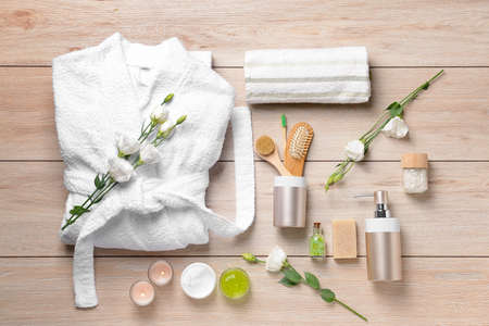 Clean bathrobe with spa supplies on wooden background