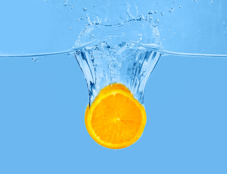 Falling of orange piece into water on light backgroundの写真素材