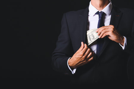Businessman putting bribe in pocket against dark background. Concept of corruptionの写真素材