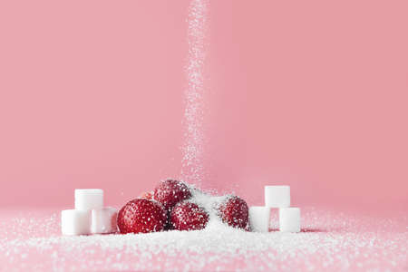 Sprinkling of sugar onto fresh strawberries against color background